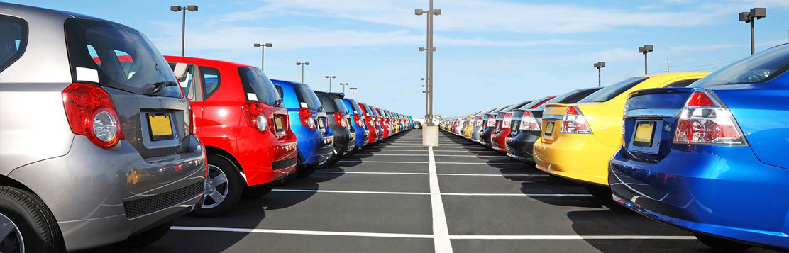 Filas de automóviles de diferentes colores estacionados en un amplio lote al aire libre, bajo un cielo despejado. La imagen muestra una vista simétrica de los vehículos alineados, lo que indica un centro de importación de vehículos organizado